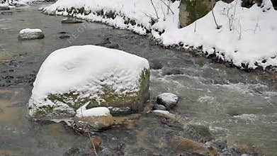 Mountain brook with a boulder at winter time. Slow motion
