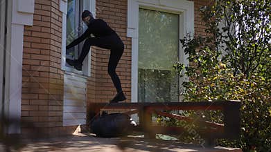 Girl thief in black mask throws stolen bag, suitcase with valuables from window