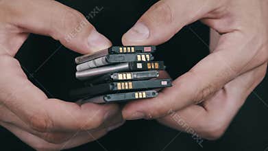 Close-Up of a Man Holding Various Used Smartphone Batteries.