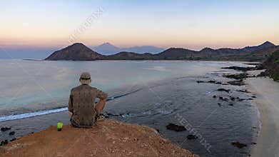 lone traveler sitting on a cliff by the indian ocean with a view to a huge volcano in eastern Indonesia