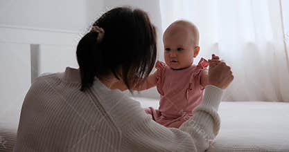 Mother doing gentle arm exercises with infant daughter on bed