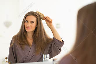 Happy young woman combing hair in bathroom