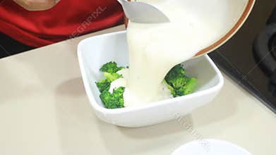 Mix broccoli with liquid flour. someone pours liquid flour into a bowl containing broccoli
