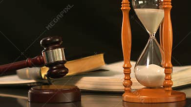 Gavel dropping on sounding block beside hourglass and bible