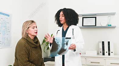 Diverse Female Doctor Explains X-Ray Results to Senior Patient During Medical Consultation at Clinic