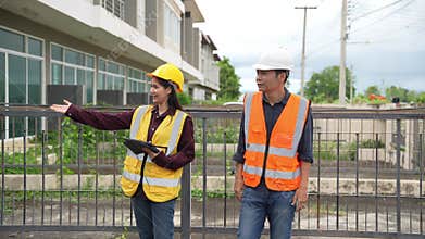 Two civil engineers inspecting a project, an Asian female architect and a male contractor wearing hard hats while holding tablets