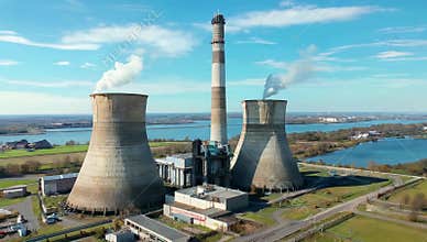 Aerial view of a power plant with cooling towers and a tall smokestack on a sunny day near water