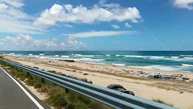 Scenic coastal road view with blue sky white clouds and sandy beach on a sunny summer day