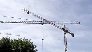 Two tall construction cranes stand against a blue sky with