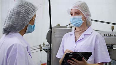 Inspector team working quality control in food processing factory, two worker woman in uniform and mask using tablet for