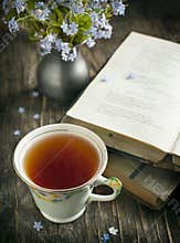 Cup of tea, vintage books and blue flowers on the table.