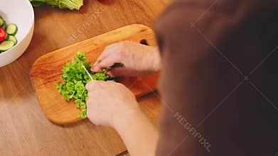 Close-up shot person hands cutting bright lettuce leaves on wooden board for healthy food vegetable diet dinner. Happy