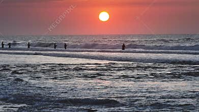 Fishermen casting lines in ocean waves at sunset on Bali