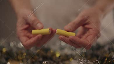 Hands holding two yellow AA batteries, getting ready to insert them into festive Christmas garland, powering holiday
