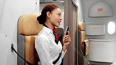 Smiling flight attendant on an airplane jumpseat speaks into a cabin intercom, preparing safety announcements inside a modern