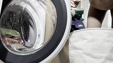 A person opens the front-load washing machine and loads