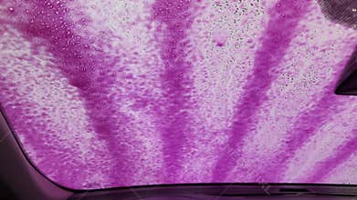 Bright pink detergent spreads across the windshield as an automatic
