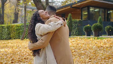 Arabian man waiting looking at wrist watch in autumn park woman coming Hispanic couple happy hugging meet talking female