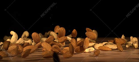 Super slow-motion of almonds and cashews fall on wooden table. Healthy snack, satisfying crunch.