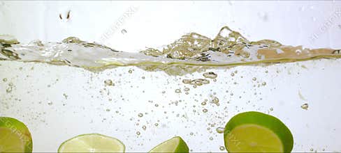 Slow-motion limes splash into water, vibrant green slices, refreshing droplets