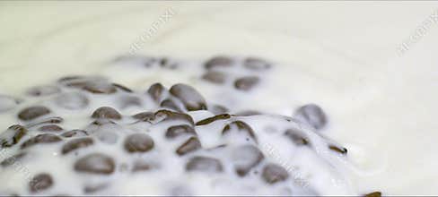 Slow-motion coffee beans falling into milk, creamy splash and swirl