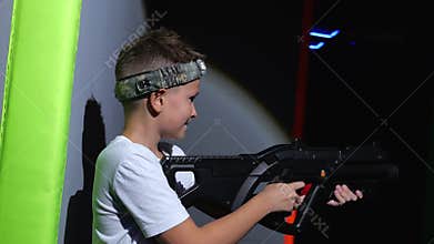 A happy teenage boy with a laser pistol is having fun in a dark laser tag arena.