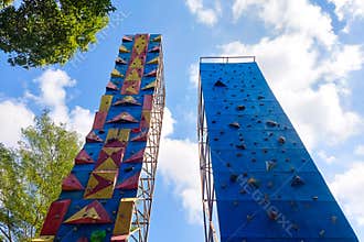 Two colorful climbing walls stand tall outdoors under a bright blue sky