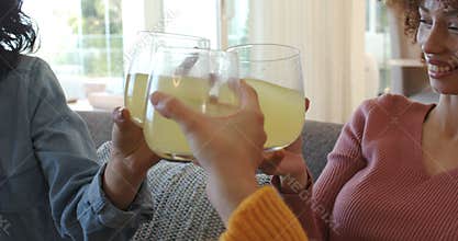 Diverse friends lifting lemonade, toasting friendship, clinking glasses before lowering on couch