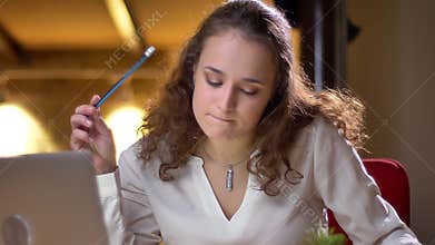 Portrait of young curly-haired woman joyfully dancing and playing invisible drums sitting in her seat in office.