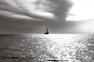 Lonely sailing vessel on horizon and a sea smooth surface in beams of sun