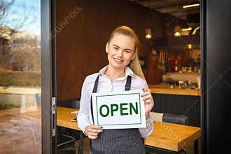 Portrait of smiling owner standing at restaurant door holding open sign, small family business