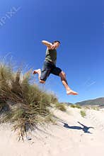 Fit, healthy middle aged man leaping over sand dunes