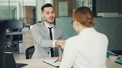Smiling young man recruiter is talking to young woman successful candidate then shaking her hand during job interview in