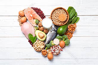 Heart shape made of natural food high in protein on white wooden background