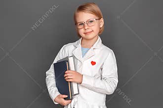 Freestyle. Little girl in lab coat and glasses isolated on grey with books smiling friendly