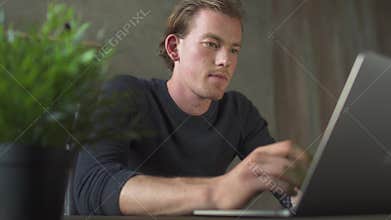Young blond worried man sitting in the office table and working at notebook. Handsome businessman typing on a laptop.