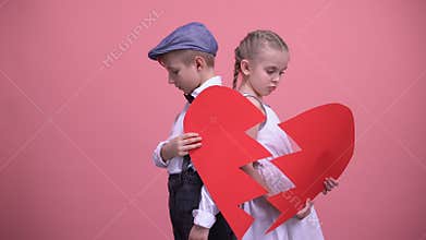 Sad little couple holding broken pieces of red heart, quarrelling, brake up