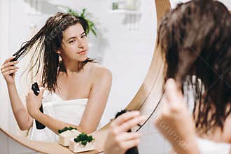 Hair and body care. Young happy woman in white towel applying conditioner mask on hair in bathroom, mirror reflection. Slim