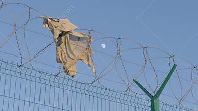 Ripped shirt hangs on a razor wire fence erected to keep immigrants away. high barrier with barbed wire in the background of the e