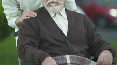 Female pushing old man in wheelchair, care and compassion in nursing, closeup