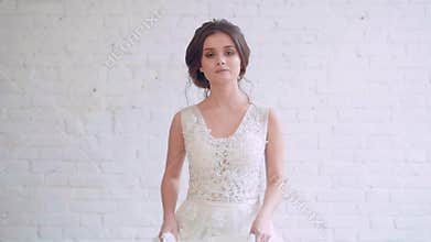 Brunette proud majestic girl with neat and gentle hairstyle in long light luxurious dress whirls and goes to the camera