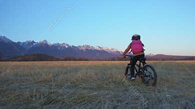 One caucasian children rides bike in wheat field. Little girl riding black orange cycle on background of beautiful snowy