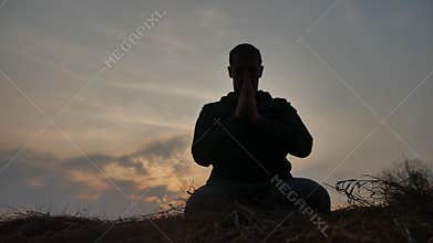 Religion concept. Silhouette of a male monk engaged in meditation lifestyle at sunset sunlight. Buddhist prayer at
