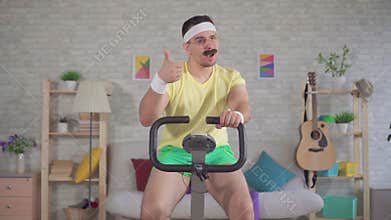 Portrait energetic man athlete from the 80`s with a mustache engaged at home on a stationary bike