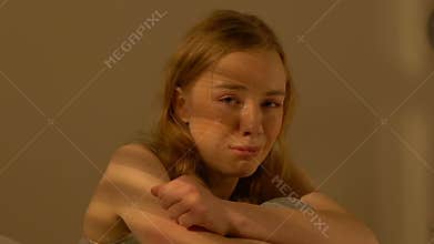 Crying teen girl sitting alone in room, helpless bullying victim violence result