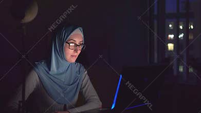 Muslim girl with glasses and a hijab with notebook in the dark