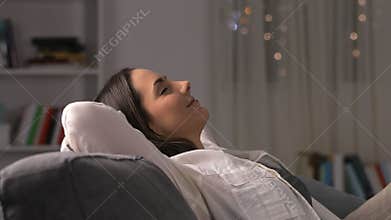 Woman leaving phone and relaxing on a couch in the night