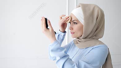 Muslim woman is applying compact powder looking at mirror.