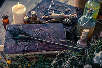A witchery stuff: multiple tincture bottles, bunches of dry healthy herbs, stack of ancient ritual books, amulets, candles...