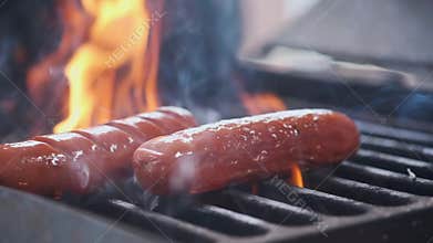 Tasty juicy sausages grilling over a fire. Cook man preparing sausages on the grill. Throws on the grill and flips over